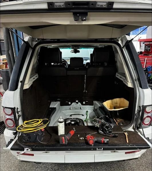 The open cargo area of a white SUV with tools, a yellow cord, and repair supplies resting on the folded tailgate.
