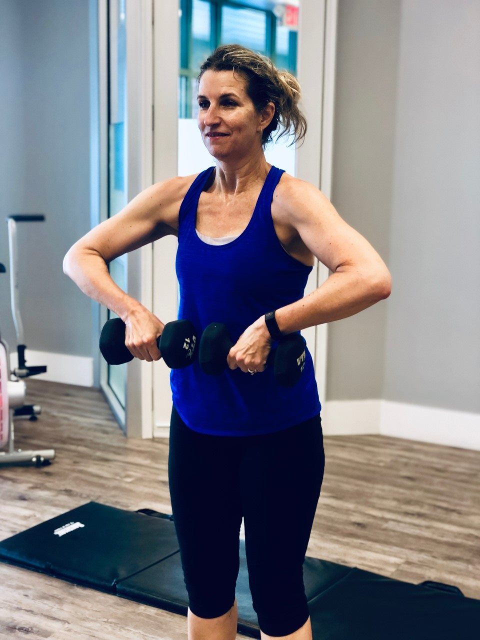 A woman in a blue tank top is lifting dumbbells in a gym.