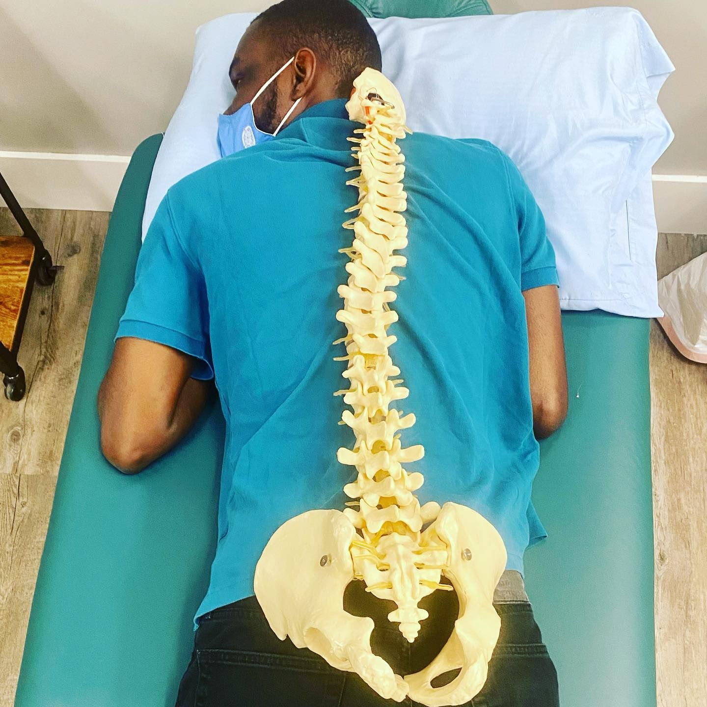 A man is laying on a bed with a model of his spine and pelvis