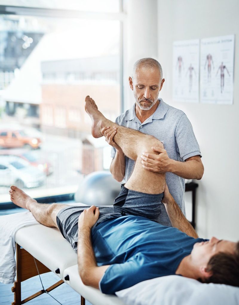A man is laying on a bed getting his leg examined by a doctor.