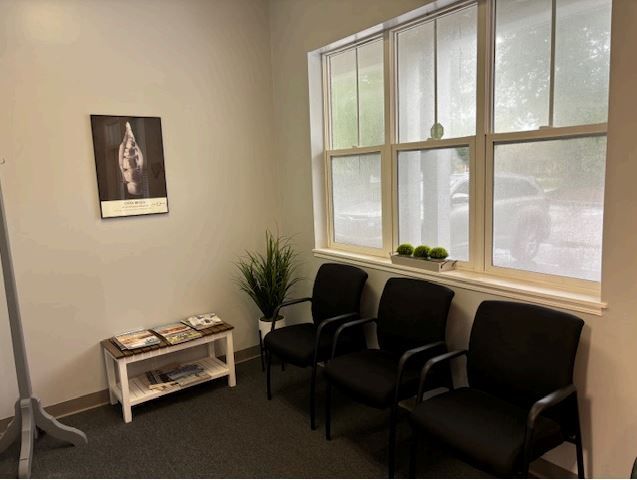 A waiting room with black chairs and a picture on the wall