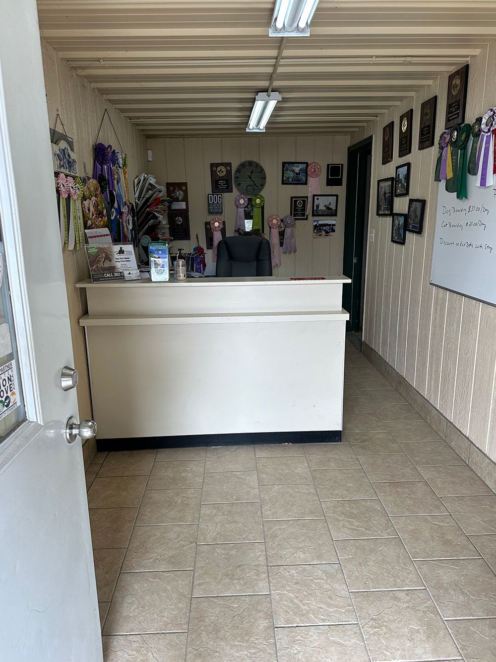 A reception area with a cream-colored desk, tile floor, and walls decorated with framed photos and ribbons.