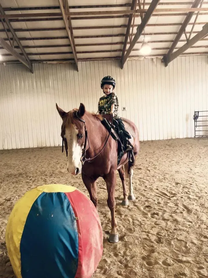 Child on horseback in an arena, with large colorful ball in foreground.