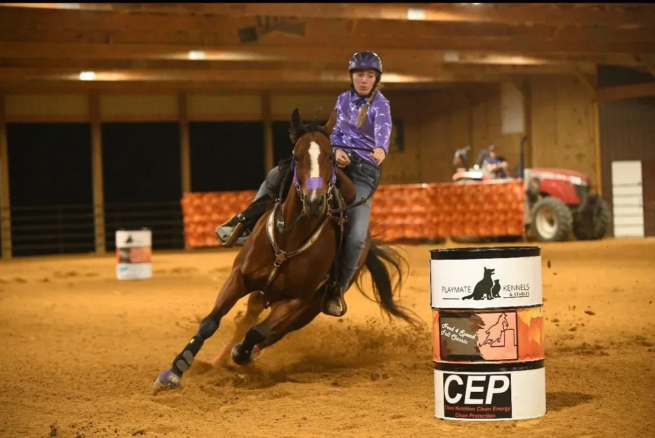 A rider on a brown horse, racing around a barrel in an indoor arena.