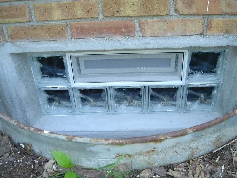 Basement window made of glass blocks, set in concrete within a metal window well.