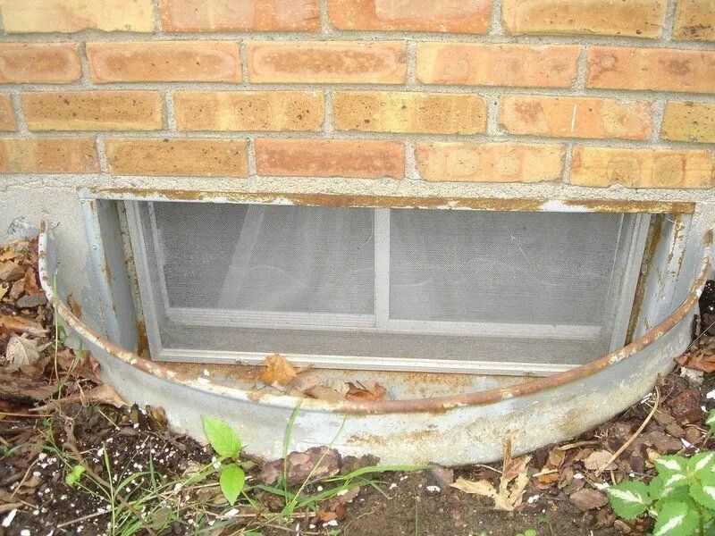 Brick foundation with a window well, metal frame, and screen.