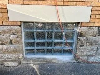 Glass block basement window with red wire against brick and stone wall.