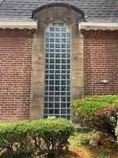 Tall, arched window of glass blocks in a brick wall.  Low bushes in front.