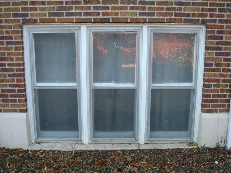 Three white-framed windows set in a brick wall, with reflections visible on the glass.