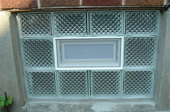 Glass block window with a small, white-framed window in the center, set in a brick wall.