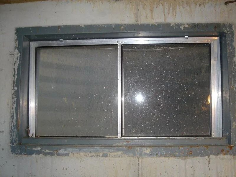 Basement window: sliding, two panes. Aluminum frame, set in concrete, stained and dirty.