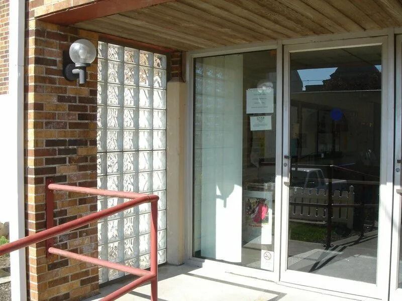 Entrance with glass block, brick wall, and glass doors. Red railing and light fixture visible.