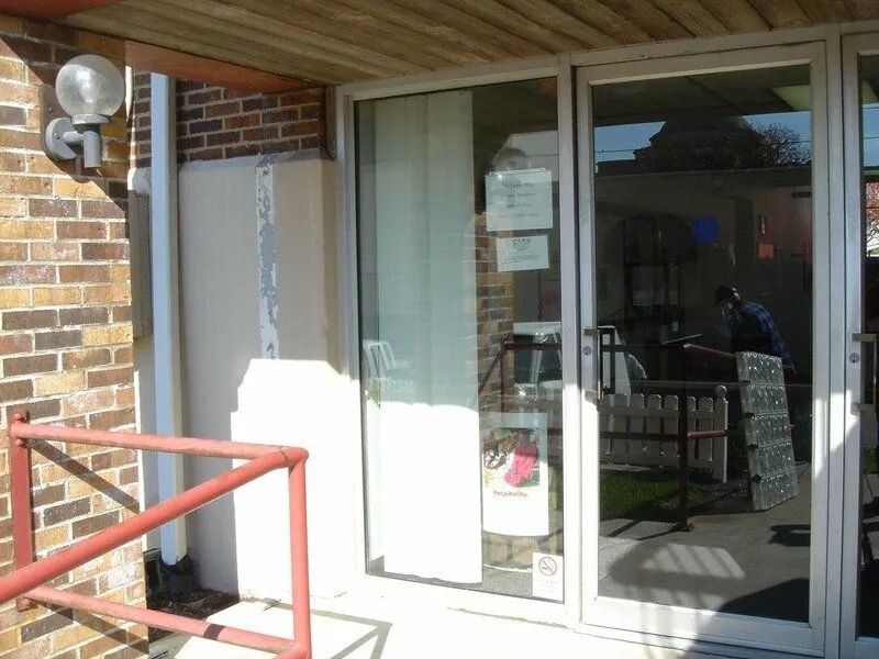 Exterior door with a white barrier next to a brick wall and a red railing.
