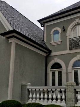 Gray stucco house with a dark roof, white trim, and a balcony with decorative railings.