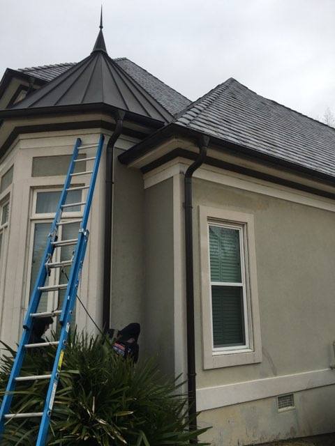 Blue ladder against a light-colored house with dark trim and roof. Overcast sky.