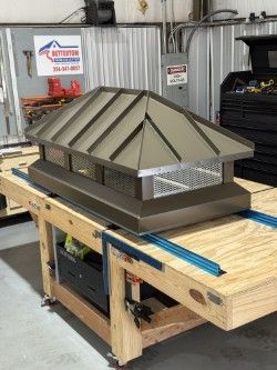 Brown chimney cap with screened sides on a wooden workbench in a workshop.