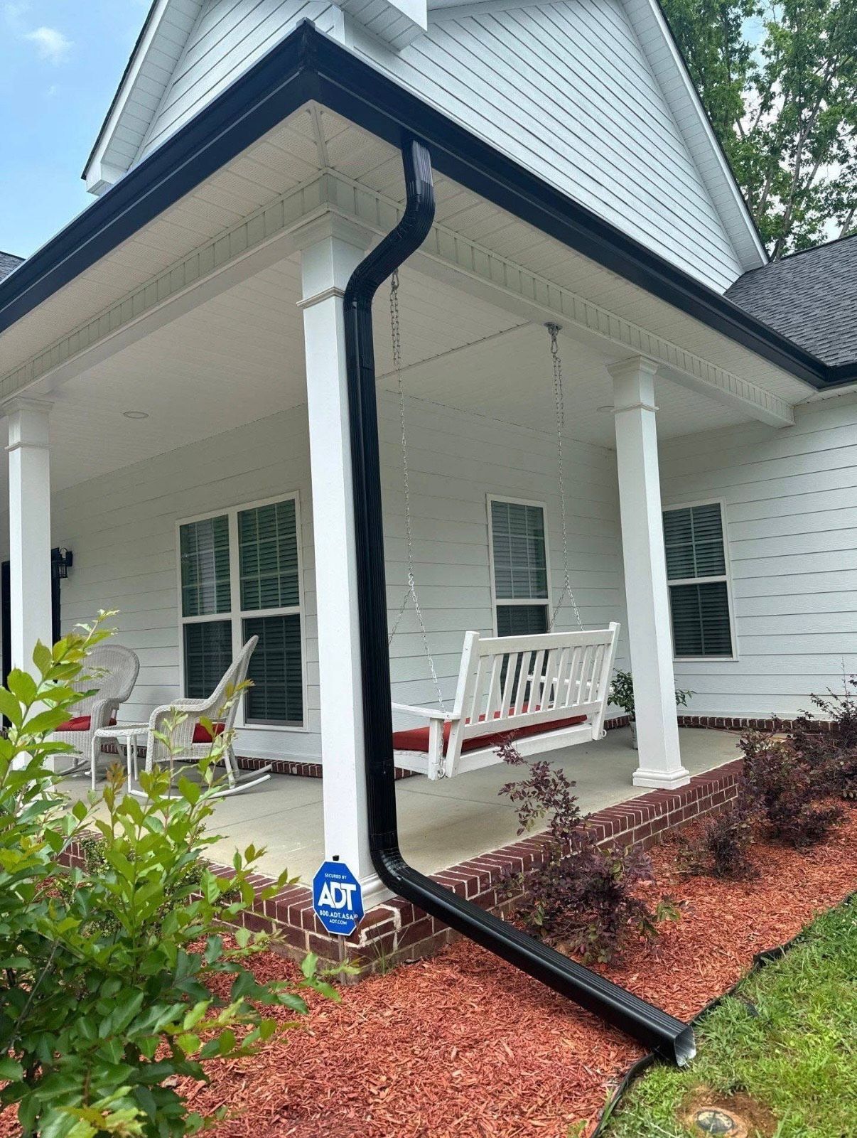 black gutter and downspout on a porch with a swing and landscaping