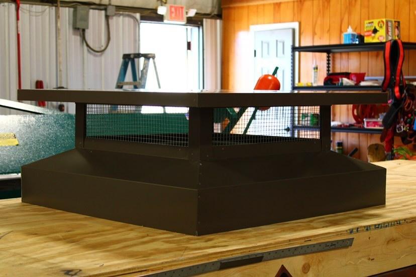Brown metal chimney cap on a wooden surface, inside a workshop.