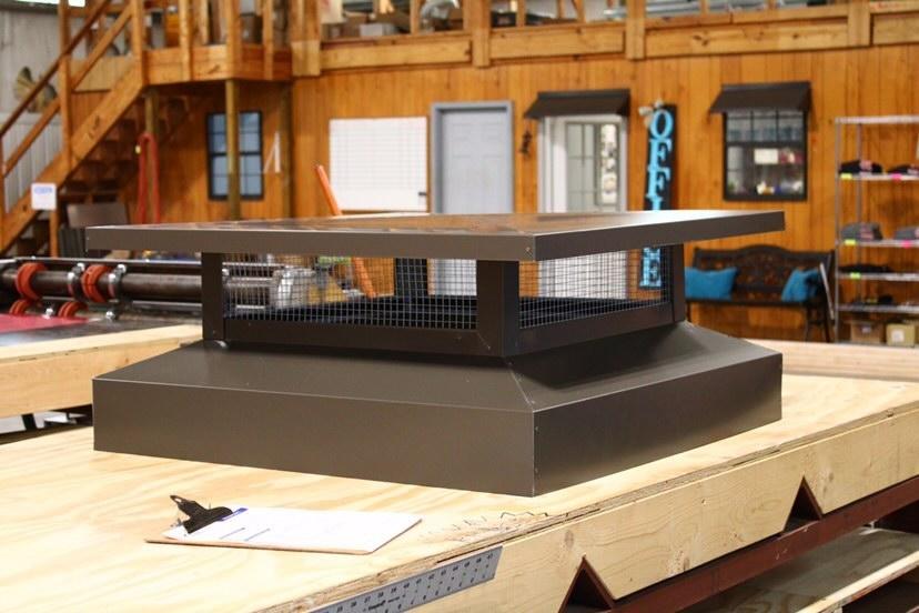 Brown chimney cap on a workbench in a workshop. Metal grate with square top.
