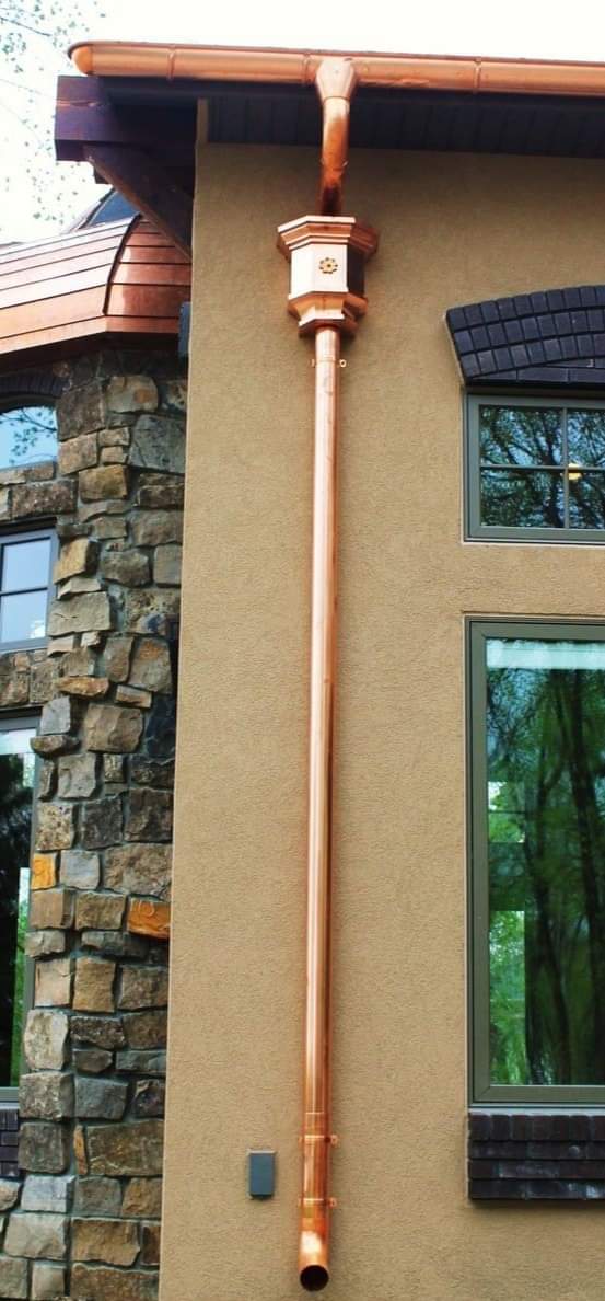 Copper gutter system on a tan stucco building, next to a stone wall.