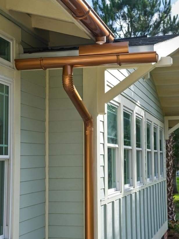 Copper gutters on a light blue house with white trim, angled towards a downspout.