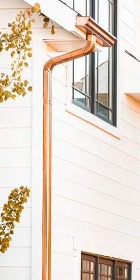 Copper gutter and downspout on a white house with black-framed windows.