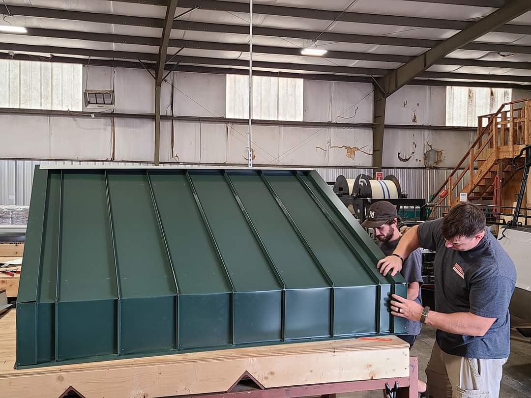 Two men installing green metal roofing in a workshop.