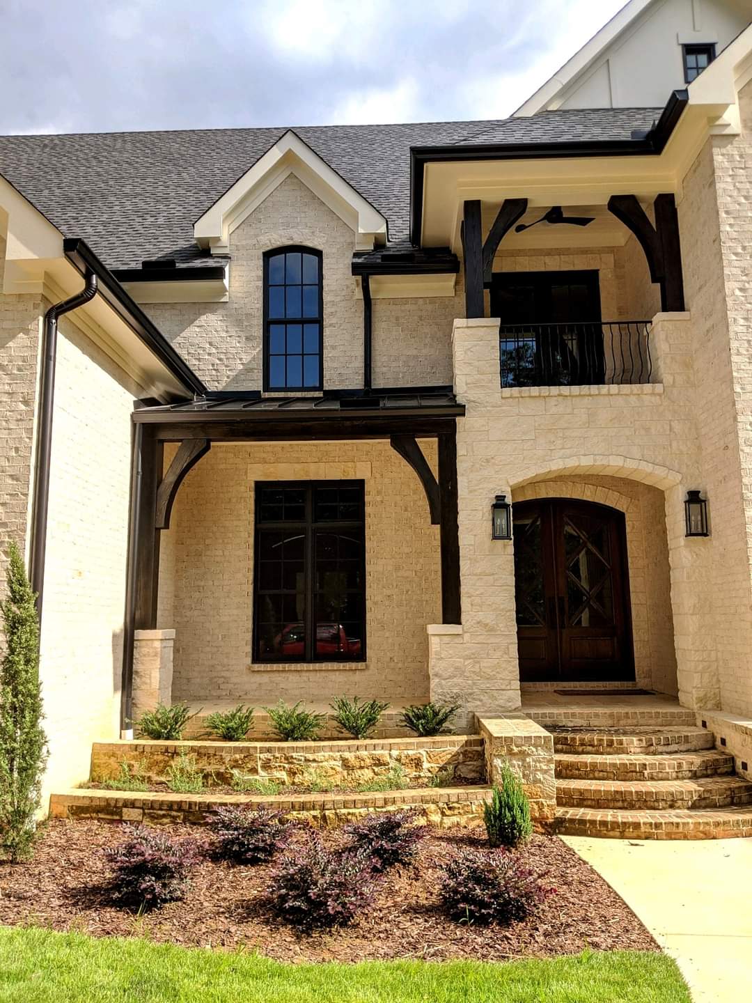 Beige brick house with dark wood accents, arched entry, and stone steps.