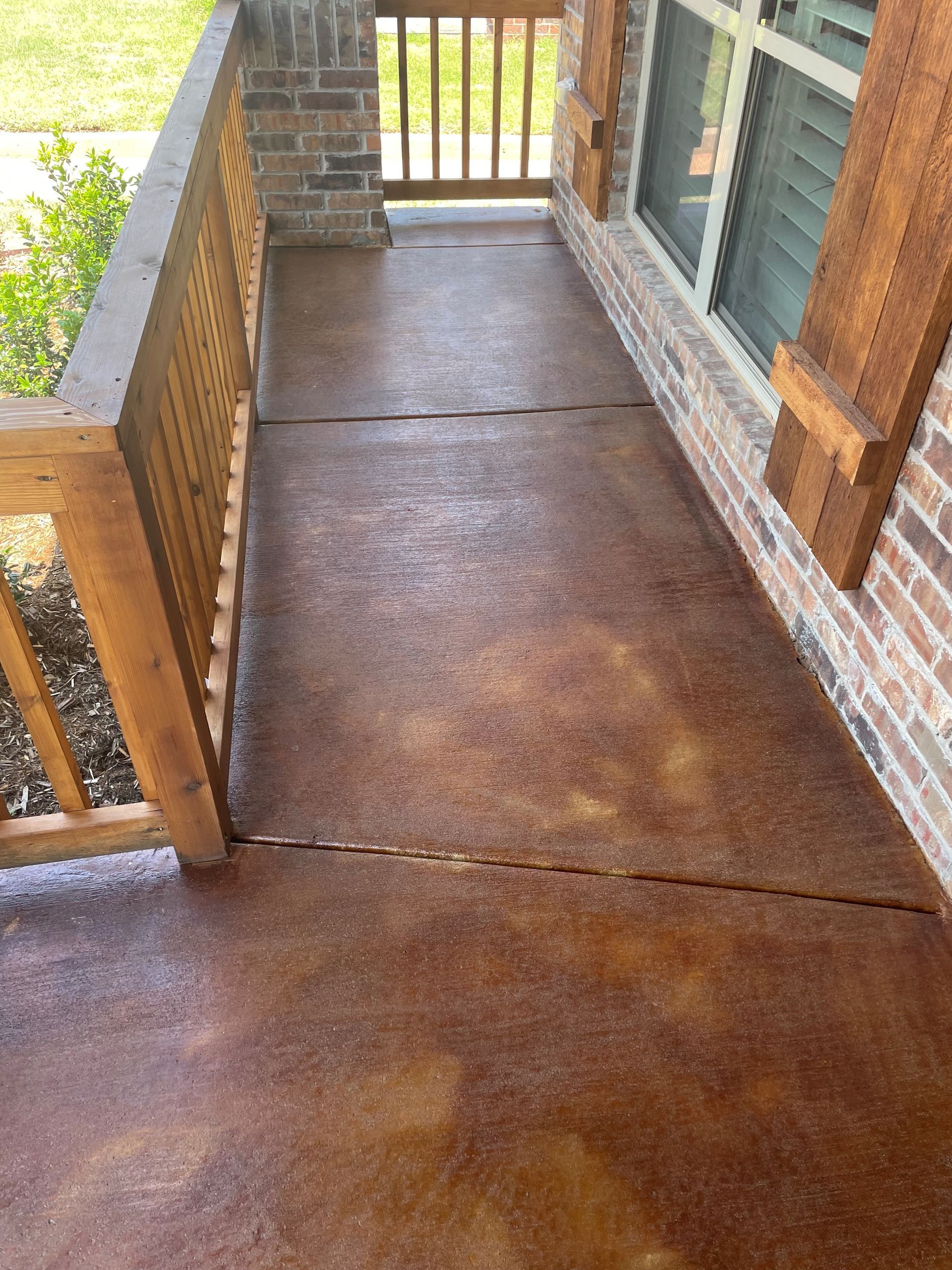 A concrete porch with a wooden railing and a brick wall.