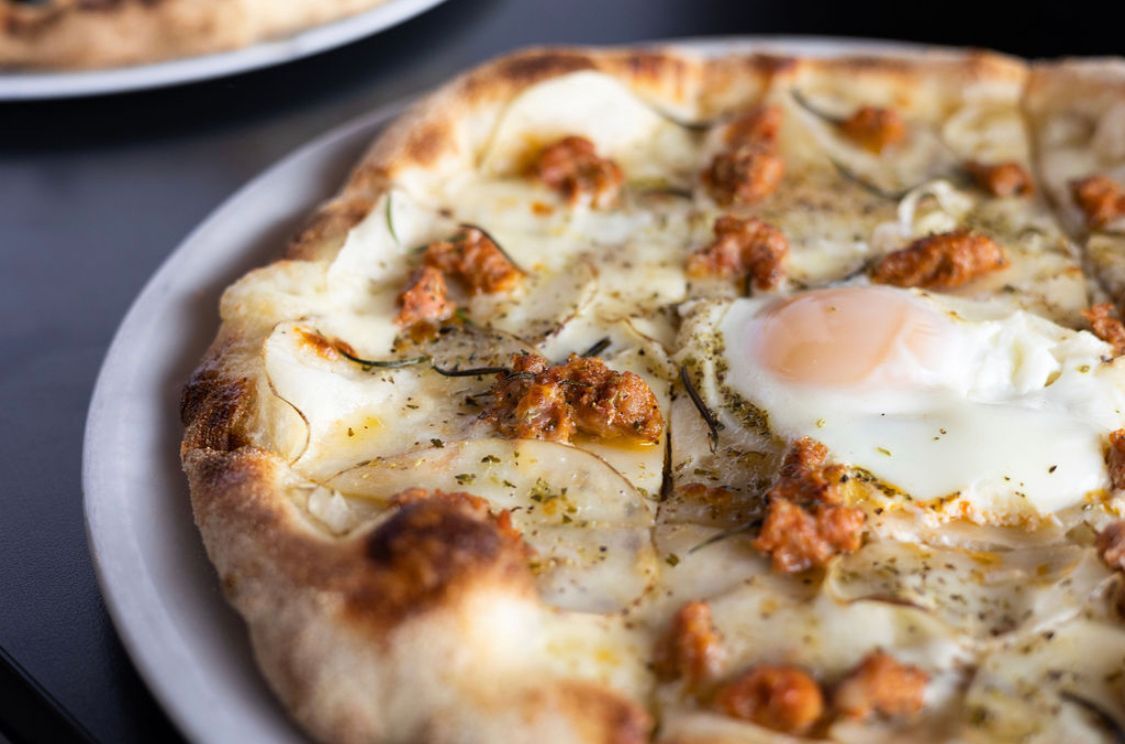 A pizza with an egg on top of it is on a plate.