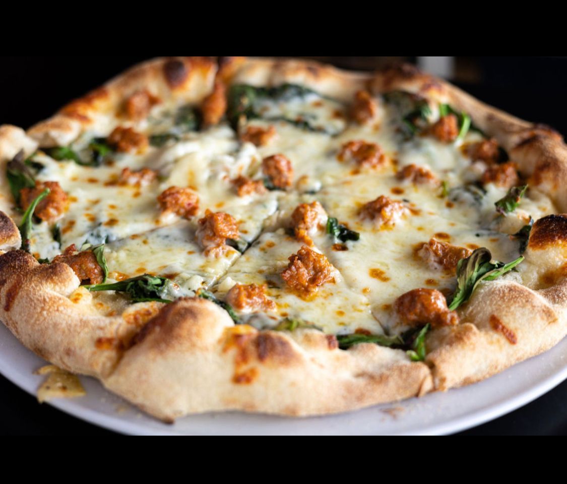 A pizza with spinach and sausage on a white plate.