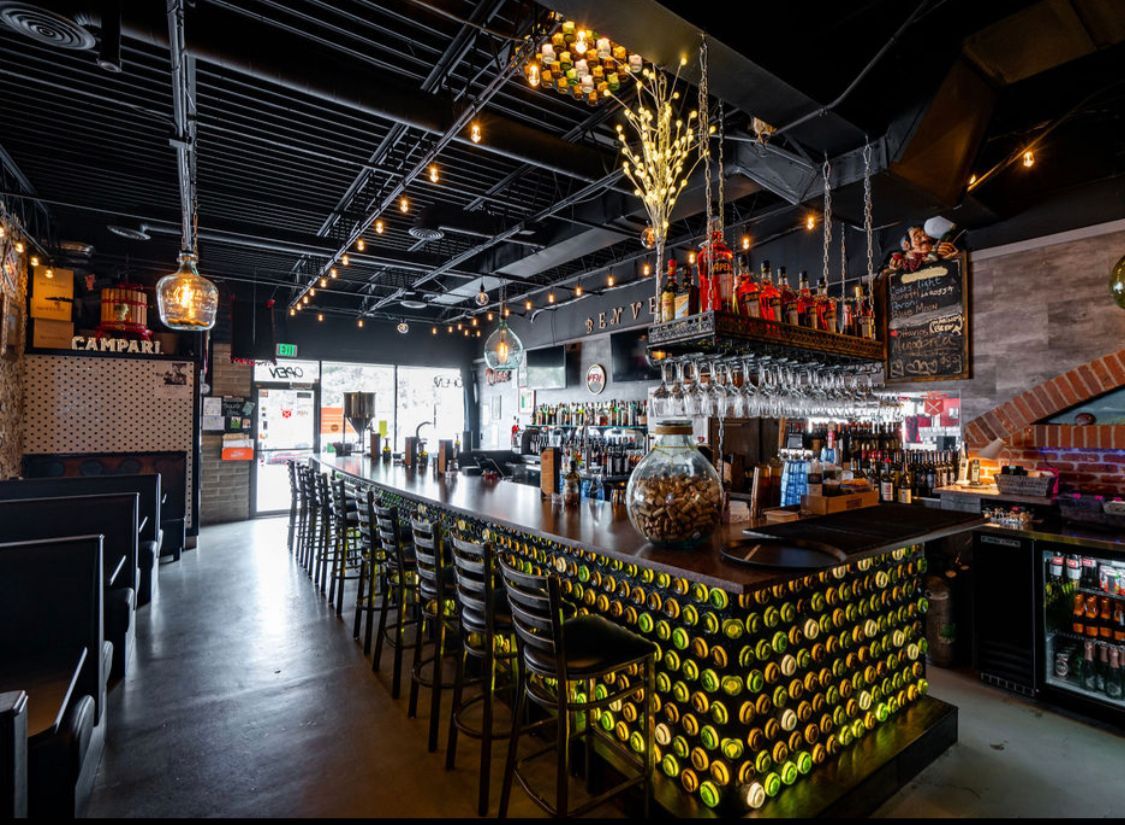 A restaurant with a long bar lined with bottles of wine.