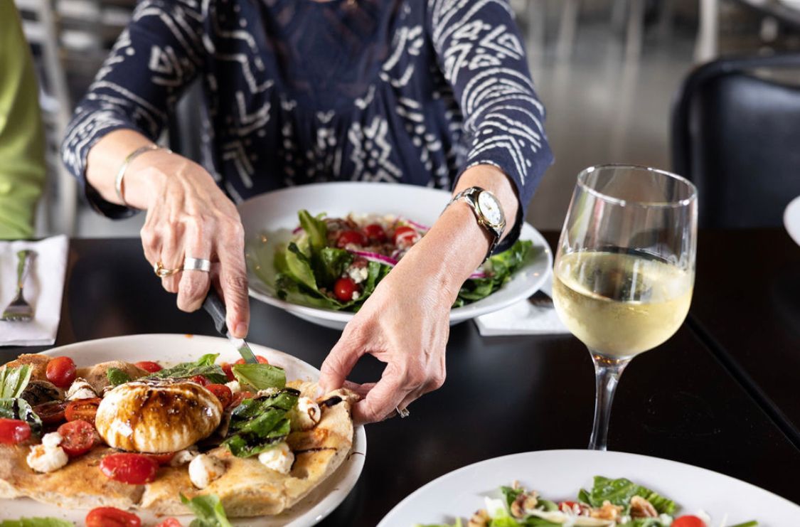 A woman is sitting at a table with plates of food and a glass of wine.