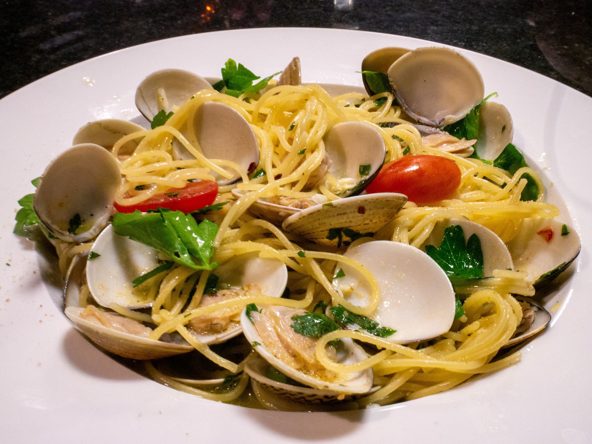A white plate topped with spaghetti, clams, and tomatoes.