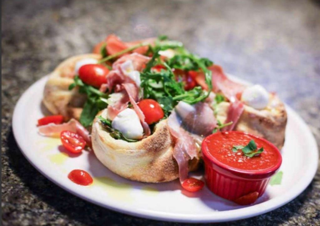 A white plate topped with pizza and tomatoes next to a bowl of sauce.