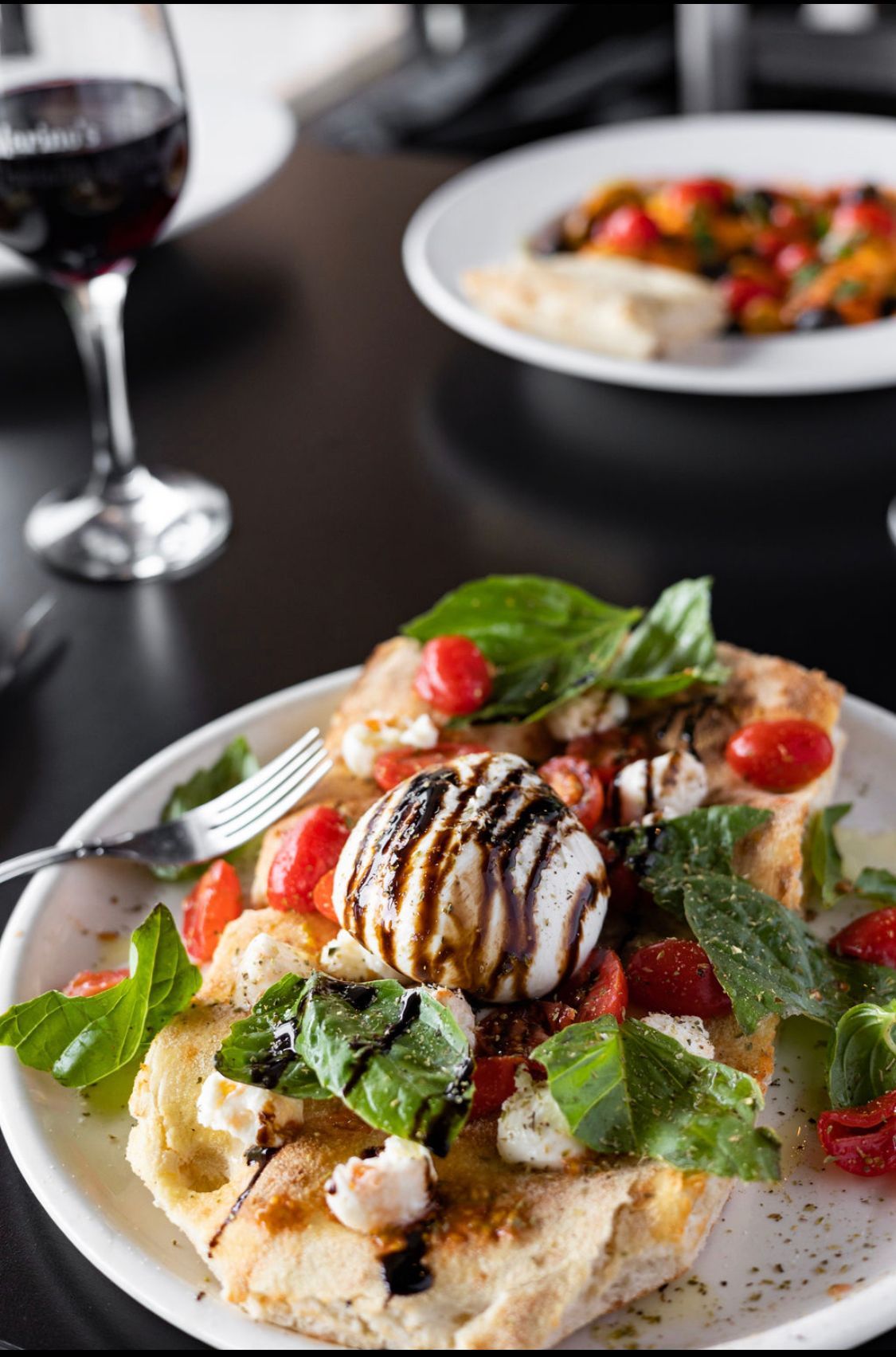 A plate of food with a fork and a glass of wine on a table.