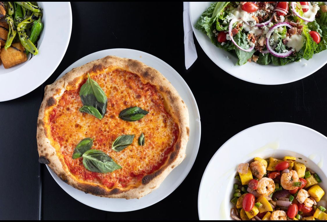 Four plates of food including a pizza and a salad are on a table.