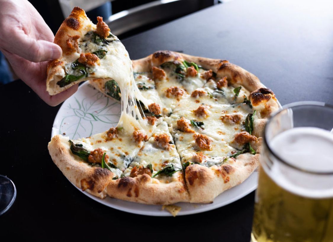 A person is taking a slice of pizza from a plate next to a glass of beer.