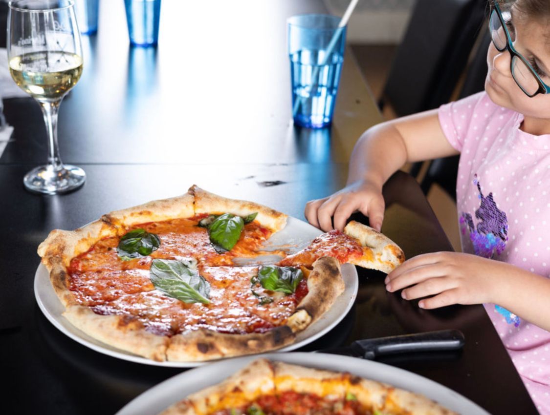 A little girl is taking a slice of pizza from a plate.