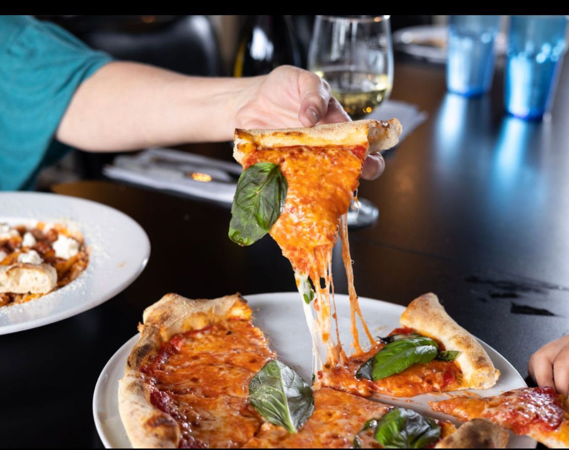 A person is taking a slice of pizza from a plate