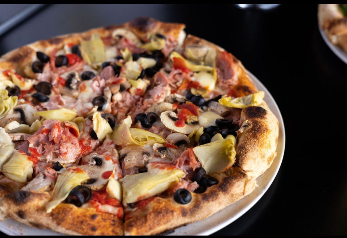 A pizza with artichokes , olives , peppers and ham on a white plate.
