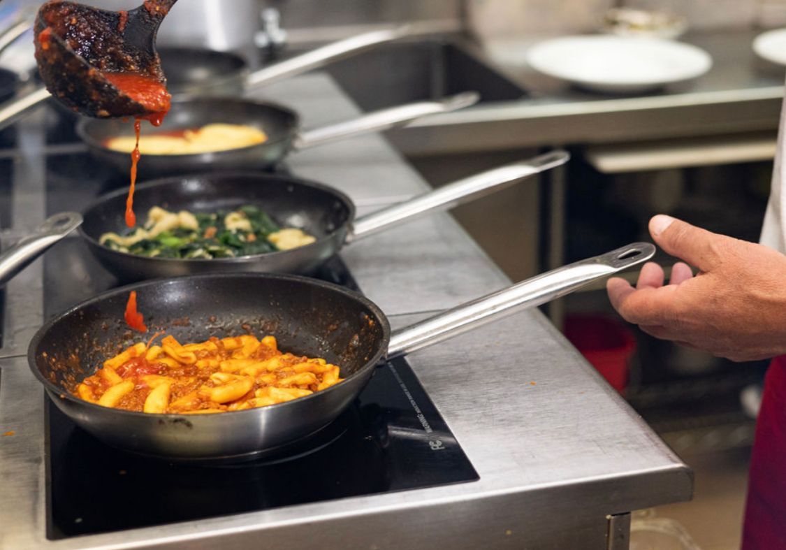 A person is pouring sauce into a frying pan in a kitchen.