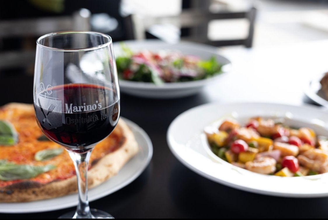 A glass of red wine sits on a table next to plates of food