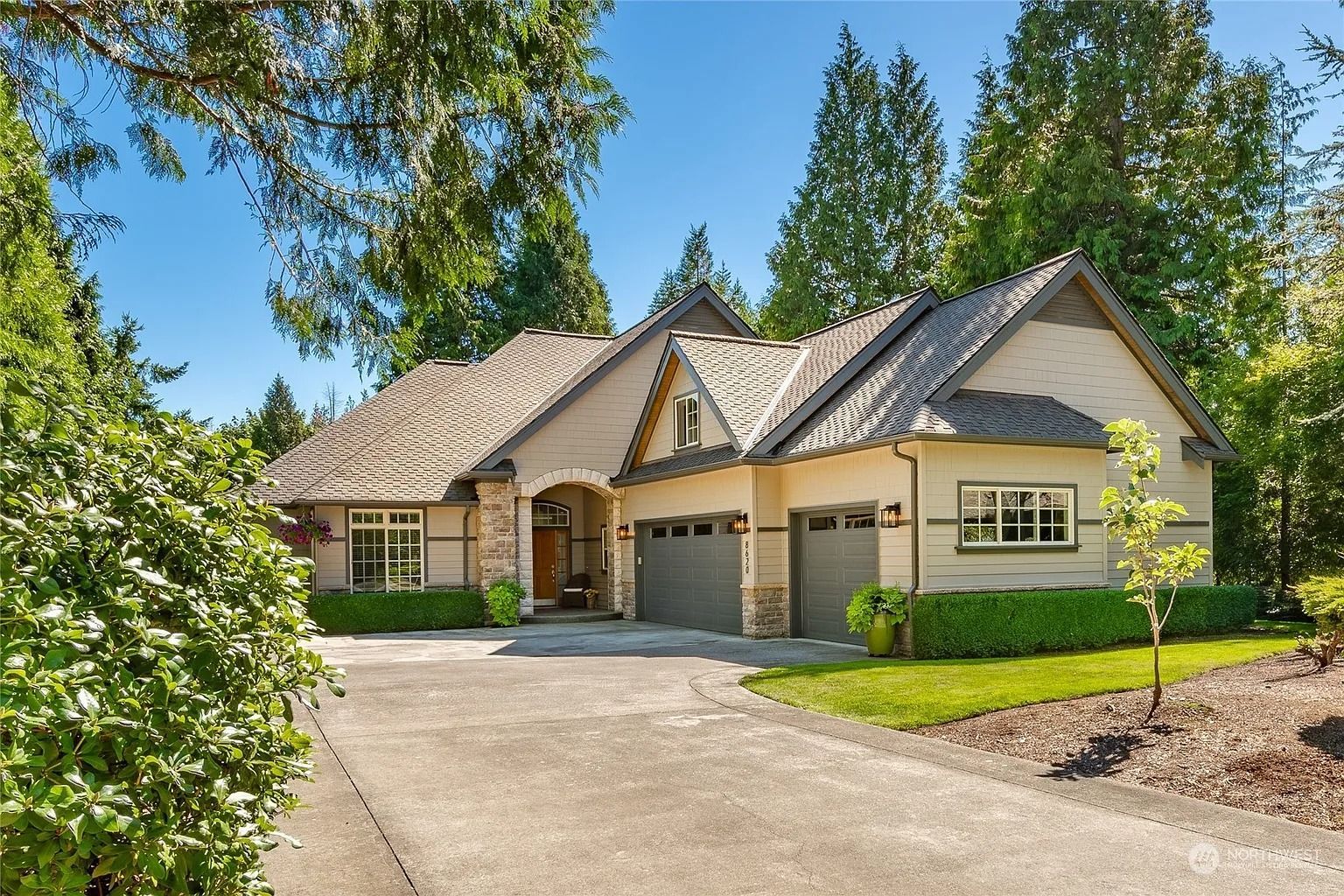 Curb-side view of a beige house with a concrete driveway, two-car garage, and a lush green lawn.