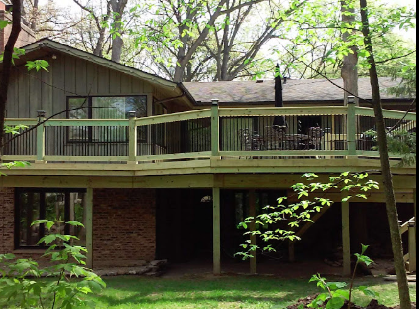 Two-story house with wooden deck; green trees frame the structure.