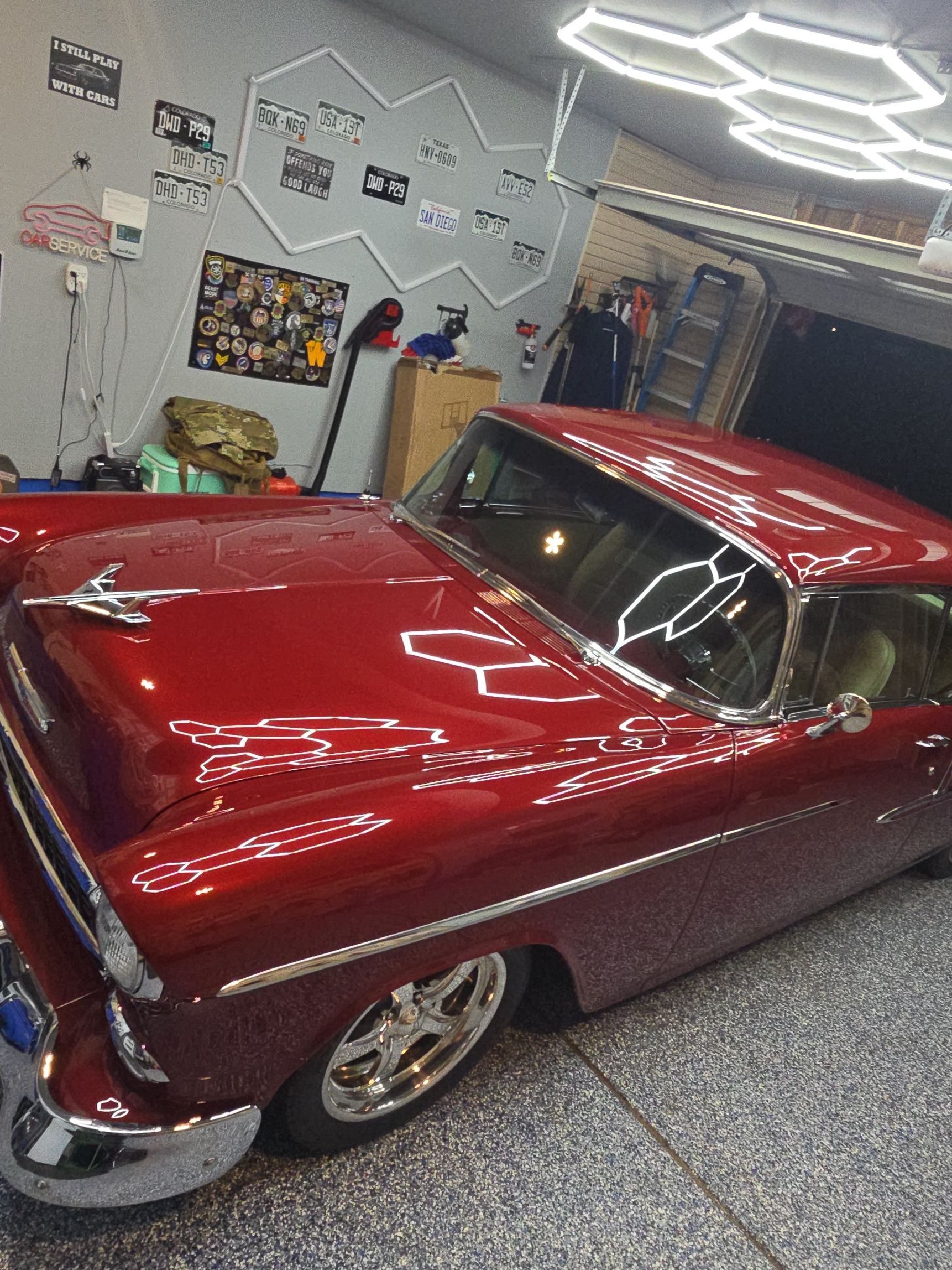 Red classic car in a garage, polished paint reflecting bright hexagon ceiling lights.