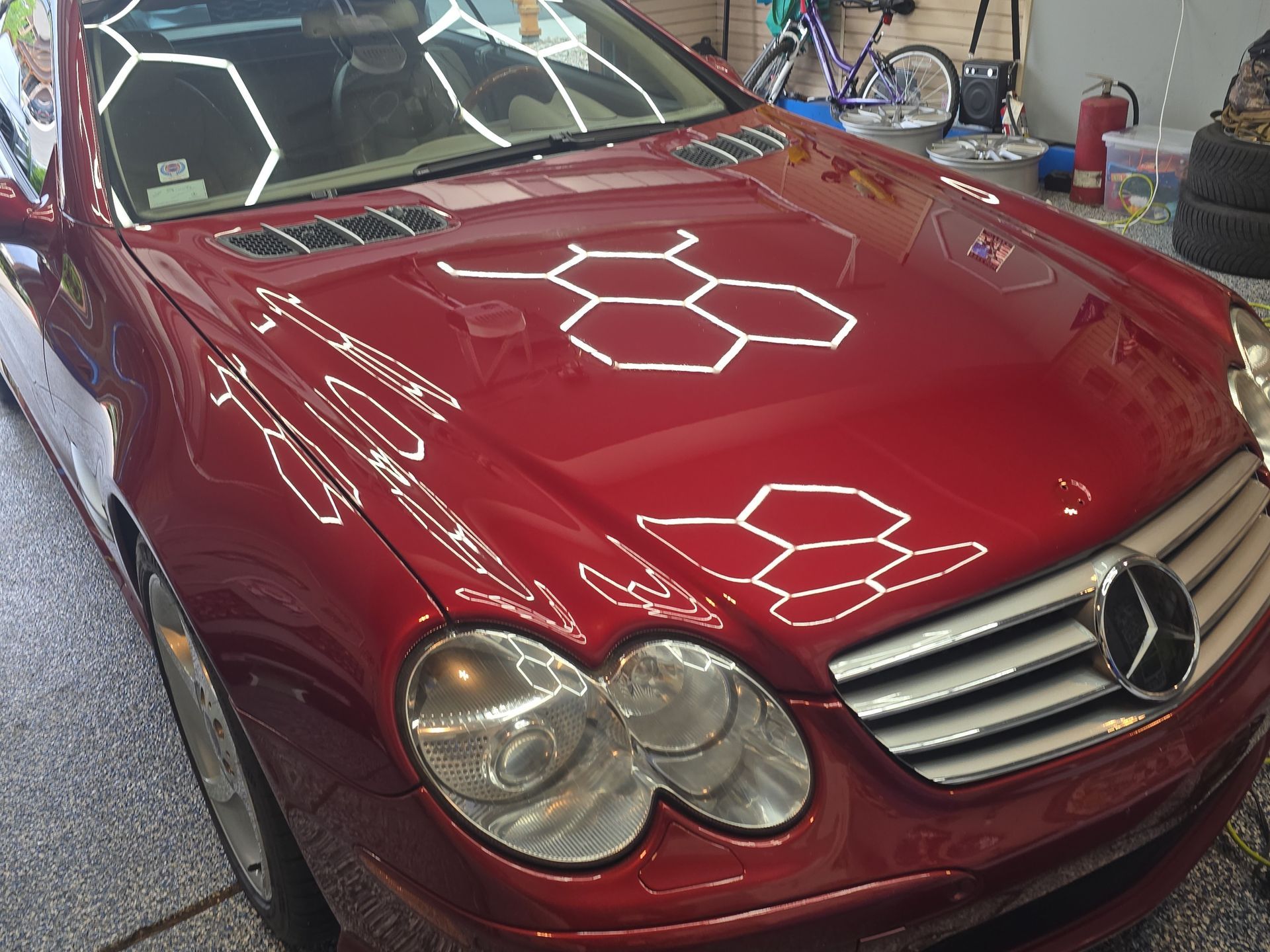 Red Mercedes car with a glossy hood in a garage, showing bright light reflections.