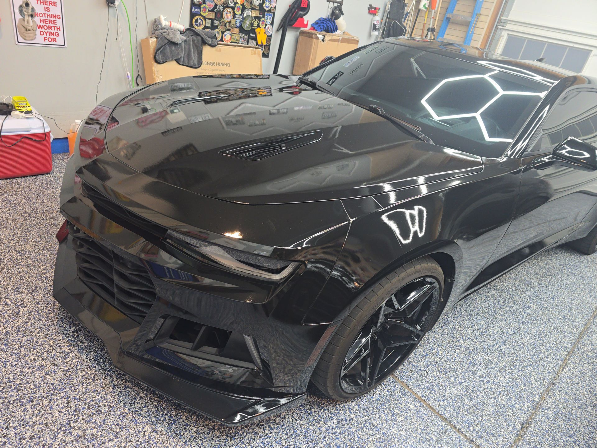 Glossy black sports car in a garage with hexagonal ceiling lights reflected on the hood