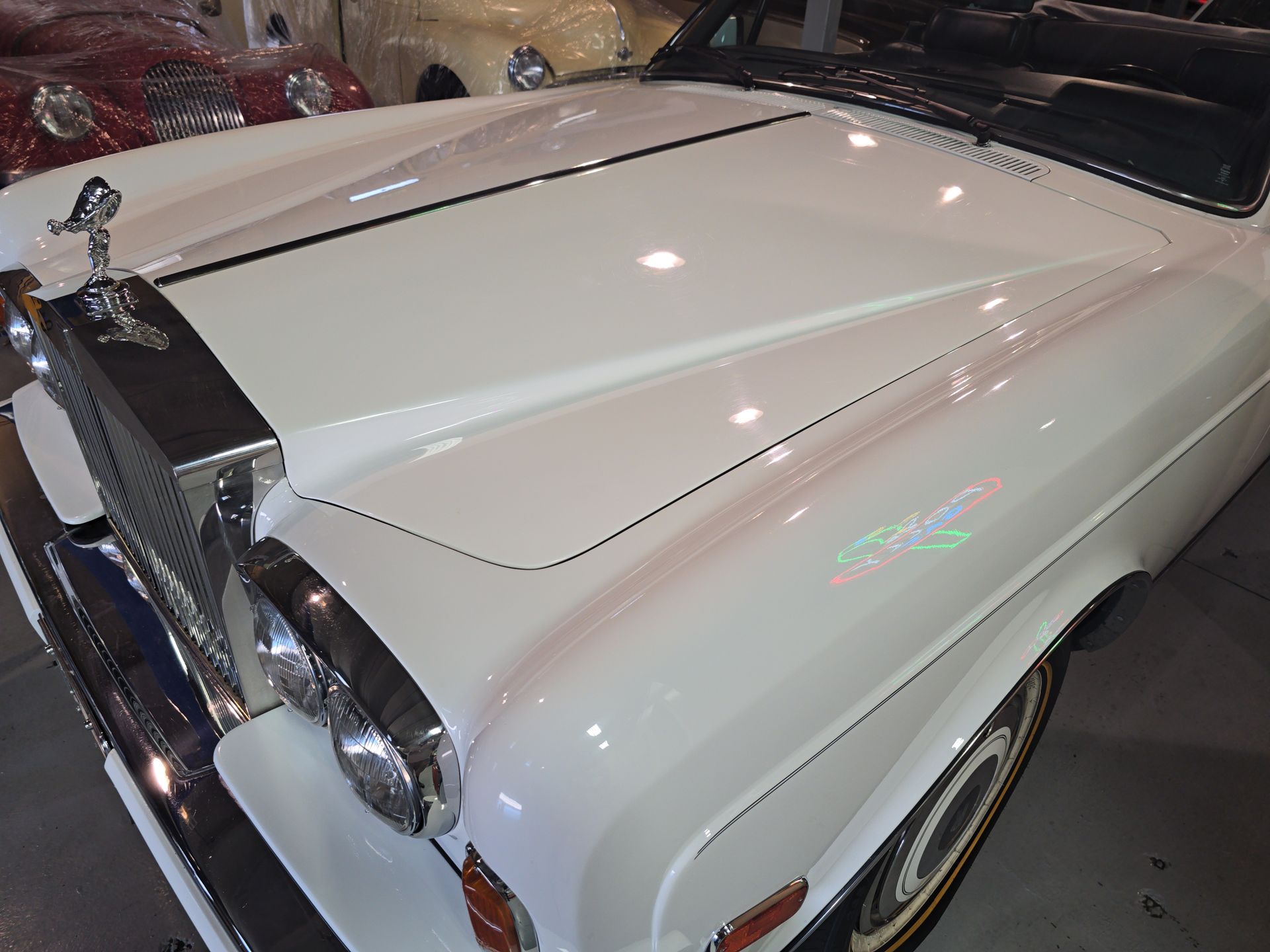 White vintage Rolls-Royce luxury car shown from the front in a showroom or garage.