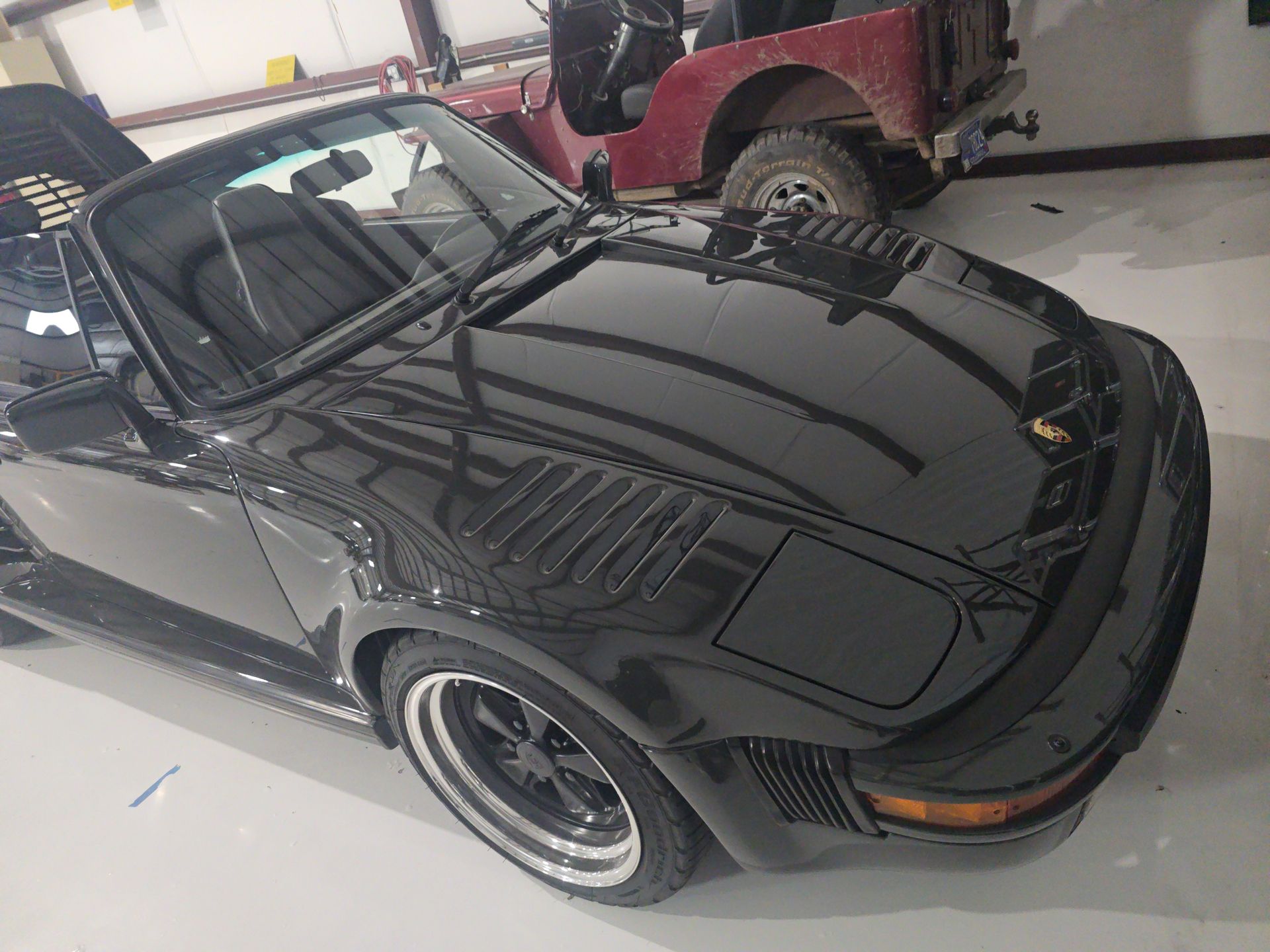 Black classic convertible sports car in a garage, viewed from the front-left side.
